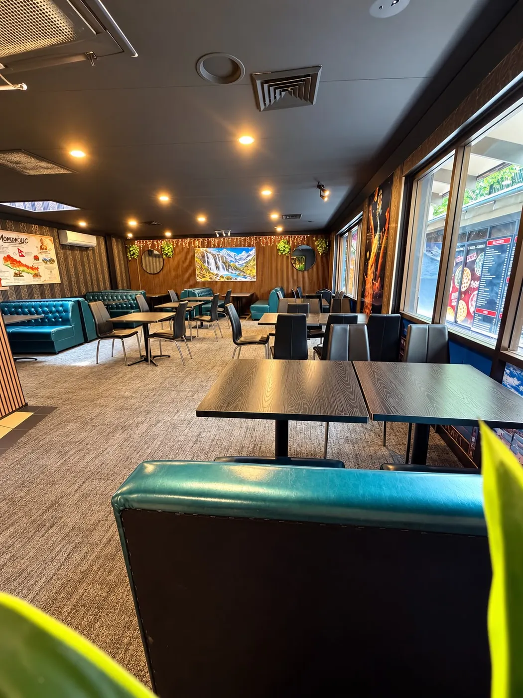 Dining room with teal tufted booths, wooden tables, a Himalayan waterfall painting and a map of Nepal on the wall